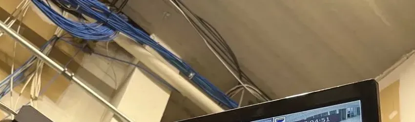 Blue cable bundles along a ceiling pipe — Mott Haven Cat6 repair reference Reference photo: loose blue and white network cable bundles strung along a metal pipe and across a beige ceiling beam above an equipment area — overhead cable route of the kind we repair in Mott Haven, Bronx