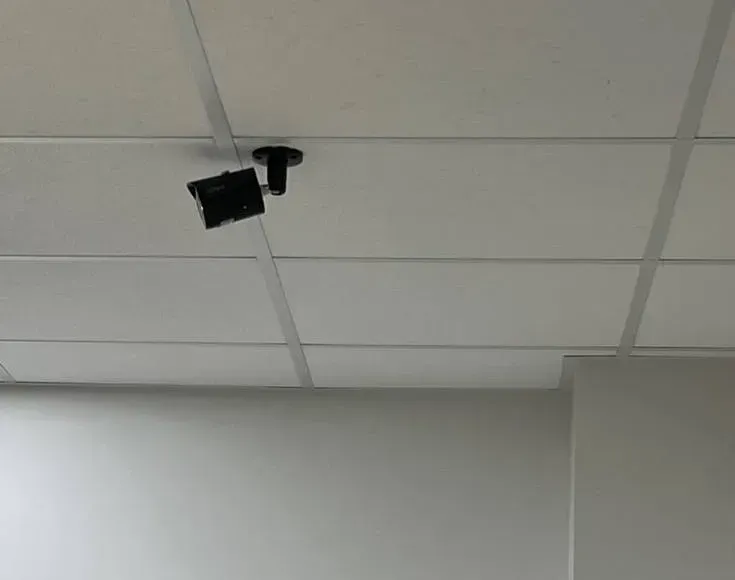 Bullet camera on a short ceiling bracket — Mott Haven Cat6 repair reference Reference photo: black bullet camera on a short bracket under a white drop ceiling above a plain wall — ceiling-mounted camera run of the kind we repair in Mott Haven, Bronx