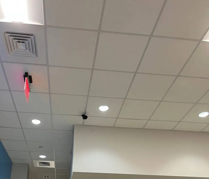 Drop ceiling with a ceiling-mounted device showing a red light, a small camera, square vents and round downlights — reference photo from another AESS job, Cat6 repair page for Tottenville, Staten Island