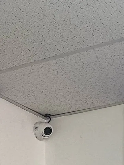 White dome camera in an office ceiling corner with its short cable loop entering the textured ceiling tile — reference photo from another AESS job, Cat6 repair page for Tottenville, Staten Island