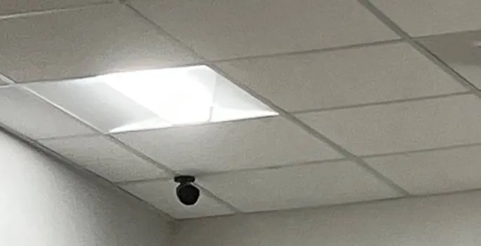 Black dome camera on a ceiling tile close to a wall corner, beside a lay-in light panel — reference photo from another AESS job, Cat6 repair page for Tottenville, Staten Island