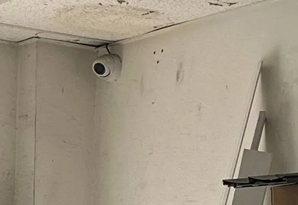 White dome camera in the corner of a storeroom under water-stained ceiling tiles — reference photo from another AESS job, Cat6 repair page for Tottenville, Staten Island