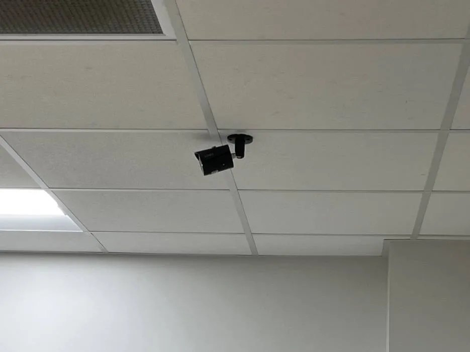 Example photo for Long Island Dahua camera installation: a small black bullet camera on a short pendant mount fixed to a white drop-ceiling grid above a plain office wall