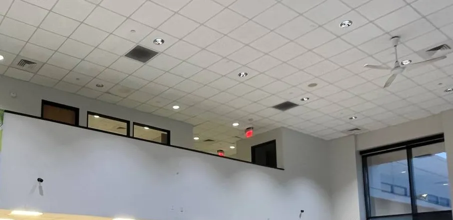 Example photo for Long Island Dahua camera installation in a large open room: two small cameras fixed high on a white wall below a mezzanine, under a grid ceiling with a ceiling fan