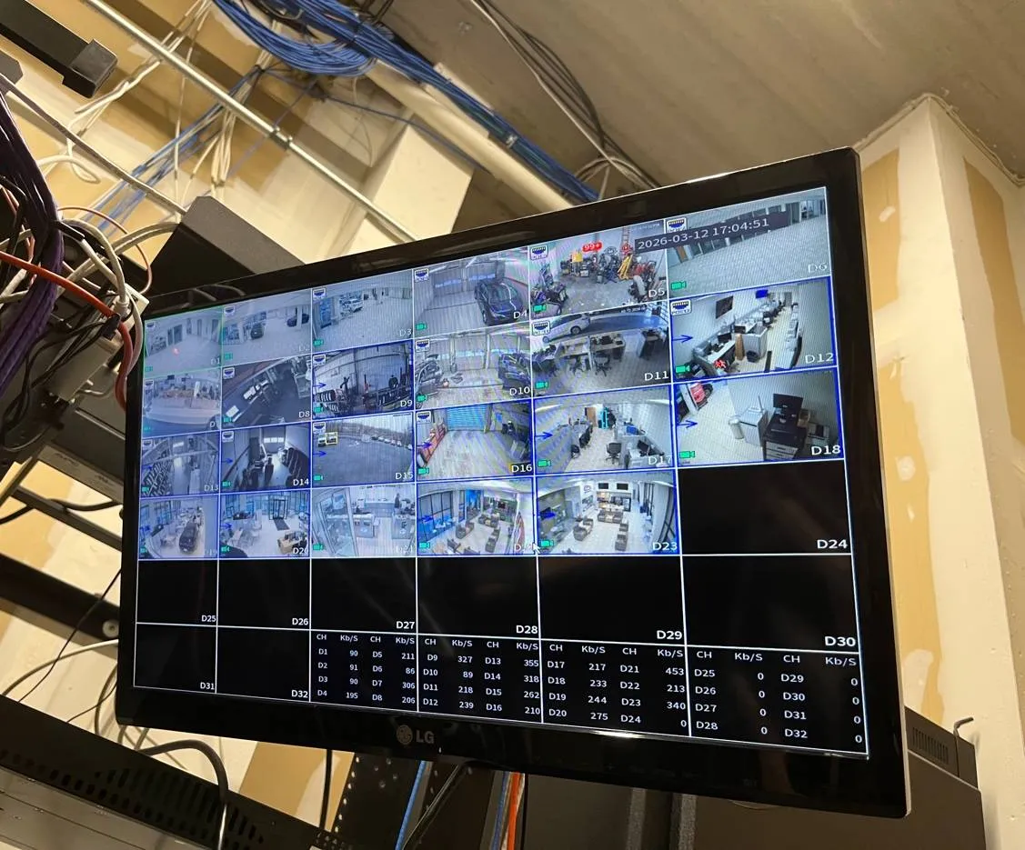 Orange County Dahua recorder room example: a monitor showing a grid of camera views and bit-rate tables, mounted beside bundles of blue, white, purple and orange network cable