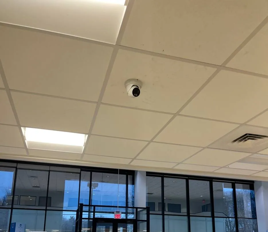 Suffolk County Dahua camera installation example photo: a white turret camera in a drop ceiling of a bright showroom, looking toward a wall of tall glass windows and an entrance door