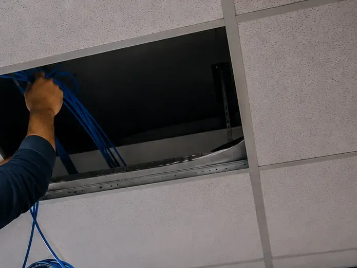 Pulling cable through an open ceiling tile — Hudson Square, Manhattan Arm reaching into an open drop-ceiling tile to pull a bundle of blue cable down from above, cable drop for fiber optic installation in Hudson Square, Manhattan