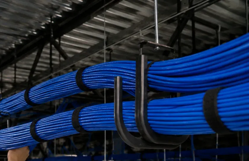 J-hook pathway under an open ceiling — Hudson Square, Manhattan Bundled blue cable supported on black J-hooks under an open ceiling structure, cable pathway for fiber optic installation in Hudson Square, Manhattan