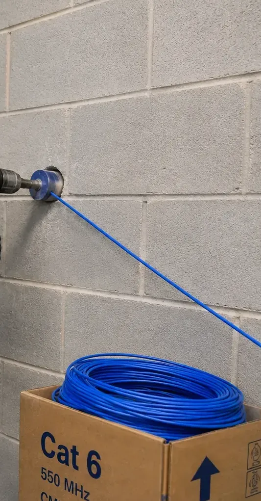 Core bit through a block wall with cable fed from a box, New Springville, Staten Island wall entry Core bit drilling through a concrete block wall with blue cable fed from a box on the floor, wall entry work for New Springville, Staten Island garage and house links