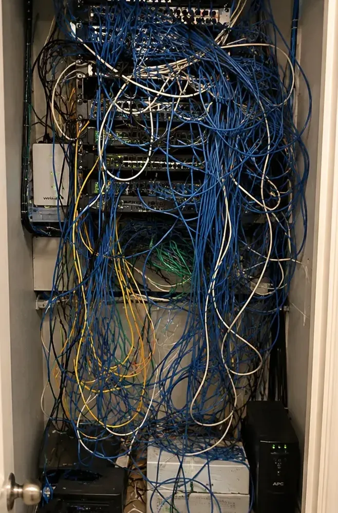 Tangled wiring closet before cleanup, New Springville, Staten Island old wiring Wall closet packed with tangled blue and white cables over unlabelled equipment before cleanup, the kind of old wiring found in New Springville, Staten Island strips