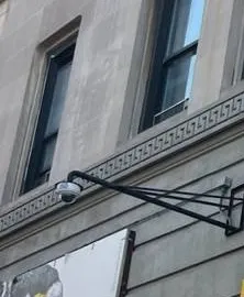 Dome camera on a wall arm on a stone facade â Manhattan Hik-Connect support example Manhattan Hik-Connect app support example photo: a white dome camera hanging from a black metal wall arm on a grey stone building facade below upper-floor windows
