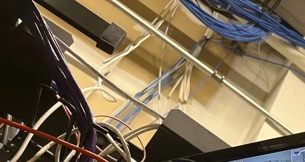 Network cables bundled along a ceiling pipe â Manhattan Hik-Connect support example Manhattan Hik-Connect app support example photo: bundles of blue and white network cables running along a metal pipe at a ceiling above an equipment rack, with a corner of a monitor at the bottom right