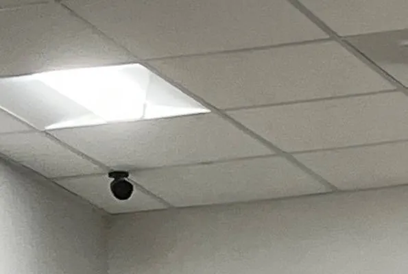 Small dark dome camera at a drop-ceiling corner, Ulster County shop example photo Hikvision camera installation Ulster County shop example: small dark dome camera at the corner of a drop ceiling beside a square light panel