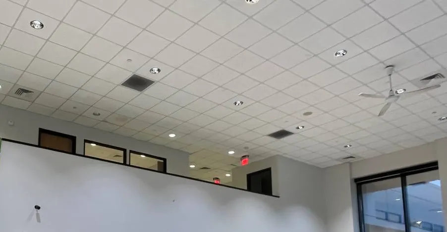 High-ceiling room with a small wall camera below a mezzanine, Ulster County example photo Hikvision security camera installation Ulster County example: high tiled ceiling with recessed lights, a ceiling fan and a small camera on the white mezzanine wall