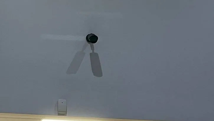 Small camera high on a tall white wall with a double shadow, Ulster County example photo Hikvision camera mounting Ulster County example: small dark camera high on a tall white wall casting a double shadow, with a motion sensor near the ceiling line below