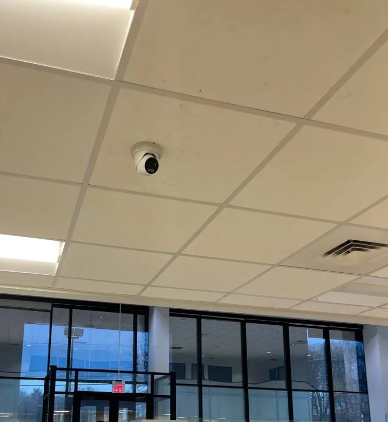 Turret camera on a tiled ceiling above a glass entry vestibule, example photo for Putnam County entry work Putnam County intercom repair example photo: a white turret camera on a drop ceiling of square tiles, with a glass entry vestibule and tall dark window frames below