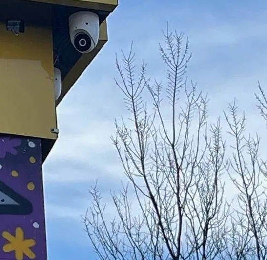 White dome camera under a shop canopy corner, example photo for Putnam County storefront entries Putnam County intercom repair example photo: a white dome camera fixed under the corner of a yellow shop canopy, with bare winter tree branches against a blue sky
