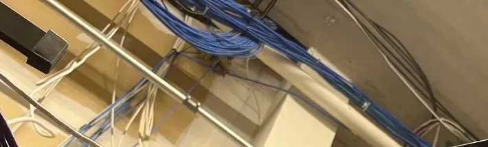Blue and white cable bundles along a ceiling pipe — example photo for Staten Island riser and wiring repairs Staten Island intercom repair example photo: bundles of blue and white cable running across a ceiling along a metal rod and a white pipe