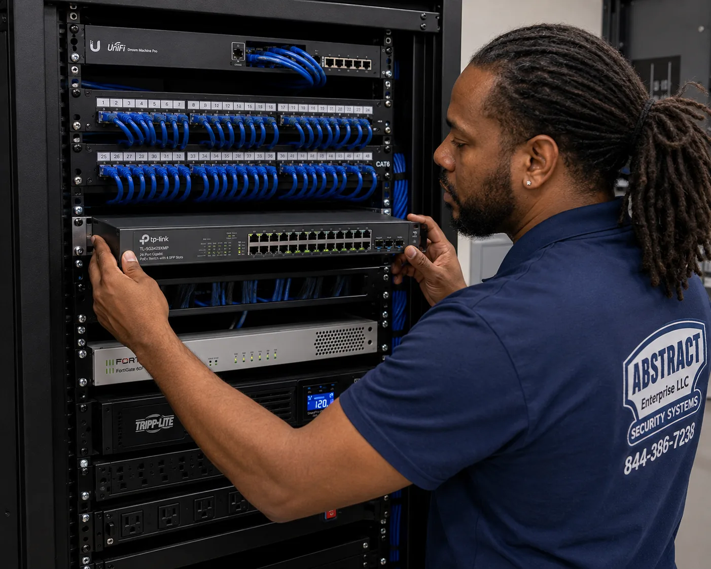 Network installation NYC technician rack-mounting a 24-port PoE managed switch below Cat6 patch panels beside a UniFi gateway and FortiGate firewall