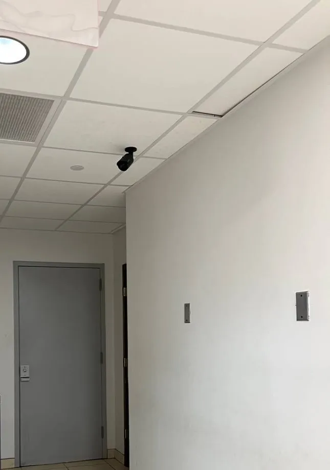 Camera aimed down a corridor to a steel door β example for Queens key rooms and recorder rooms Queens parking lot camera installation example photo: a black bullet camera at ceiling level aimed down a short tiled corridor toward a grey steel door