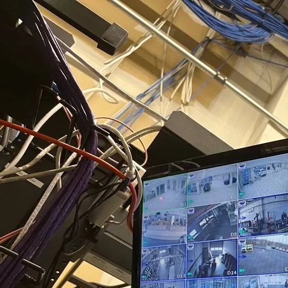 Camera cable home runs dropping into an equipment rack β example for Queens lot recorder locations Queens parking lot camera installation example photo: bundles of blue, white and purple network cable running overhead into an equipment rack beside a camera monitor