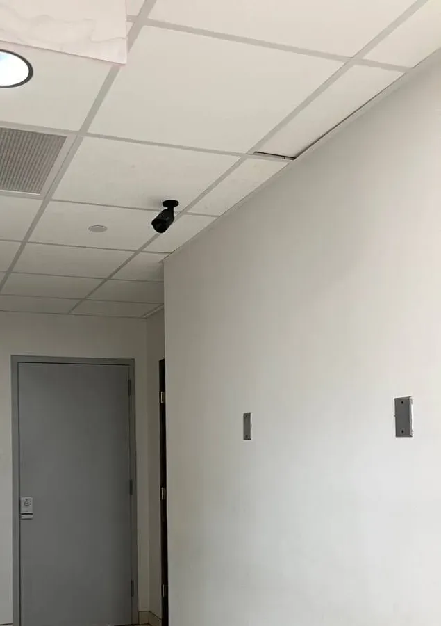 Black bullet camera on a corridor ceiling aimed at a grey door â Manhattan Smart PSS support example Manhattan Smart PSS support example photo: a small black bullet camera on a white drop ceiling in a narrow corridor, aimed at a grey door with a card reader beside it