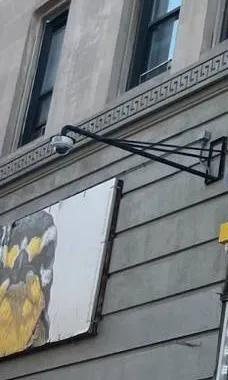 Dome camera on a steel arm under a patterned stone band â Manhattan Smart PSS support example Manhattan Smart PSS support example photo: a white dome camera on a long black steel wall arm, mounted on a grey stone facade beneath a band with a repeating key pattern and upper-floor windows