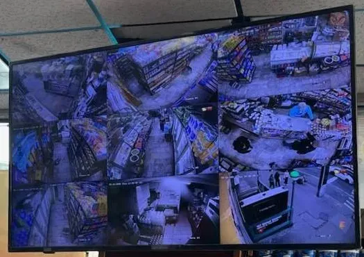 Ceiling-hung store monitor with a split-screen camera layout â Manhattan Smart PSS support example Manhattan Smart PSS support example photo: a monitor hung from a drop ceiling showing a split screen of store camera views of shelving aisles, a counter, a back room and a street entrance