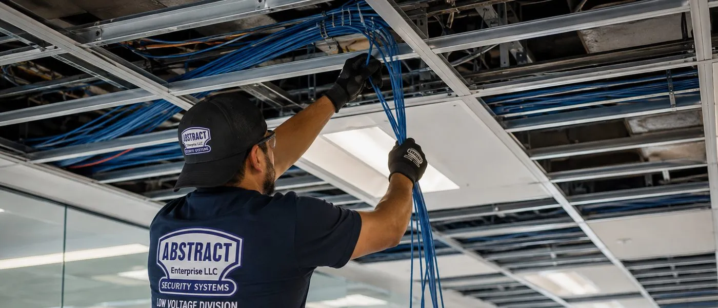 Cable bundle pulled through an open ceiling grid — Country Club, Bronx Sonos installation Sonos installation Country Club, Bronx: technician seen from behind on a ladder pulling a bundle of blue cables up through an open suspended ceiling grid