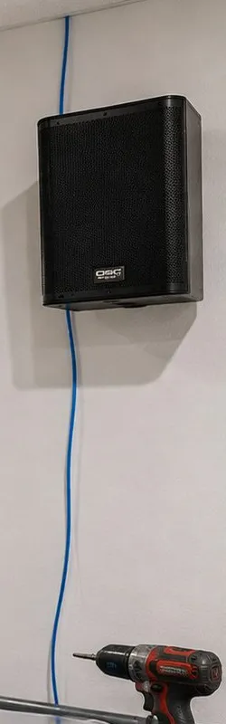 Sonos installation Forest Hills, Queens: black cabinet speaker fixed high on a pale wall with a blue cable running down the wall beneath it