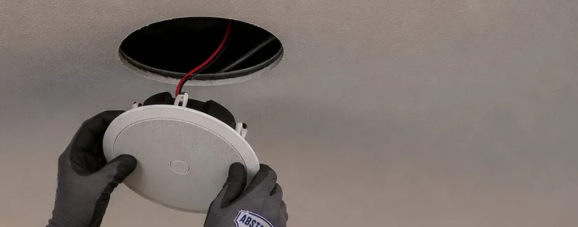 Sonos installation Great Kills, Staten Island: two gloved hands pressing a round white ceiling speaker up into a circular opening, red and black speaker wire visible inside the hole
