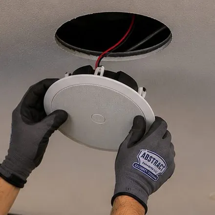 Ceiling speaker held under its cut-out — Greenwich Village, Manhattan Sonos installation Sonos installation Greenwich Village, Manhattan: grey work gloves holding a round white ceiling speaker just below a circular hole in a smooth ceiling, a red and black wire hanging from the opening