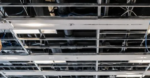 Open ceiling grid with hanging cable bundles — Greenwich Village, Manhattan Sonos installation Sonos installation Greenwich Village, Manhattan: an open suspended ceiling grid with the tiles removed, bundles of blue cable hanging from the structure above and light fittings between the rails
