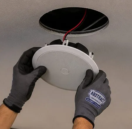 Sonos installation Long Island City, Queens: two gloved hands raising a round white ceiling speaker toward a circular opening with a red lead hanging out of it