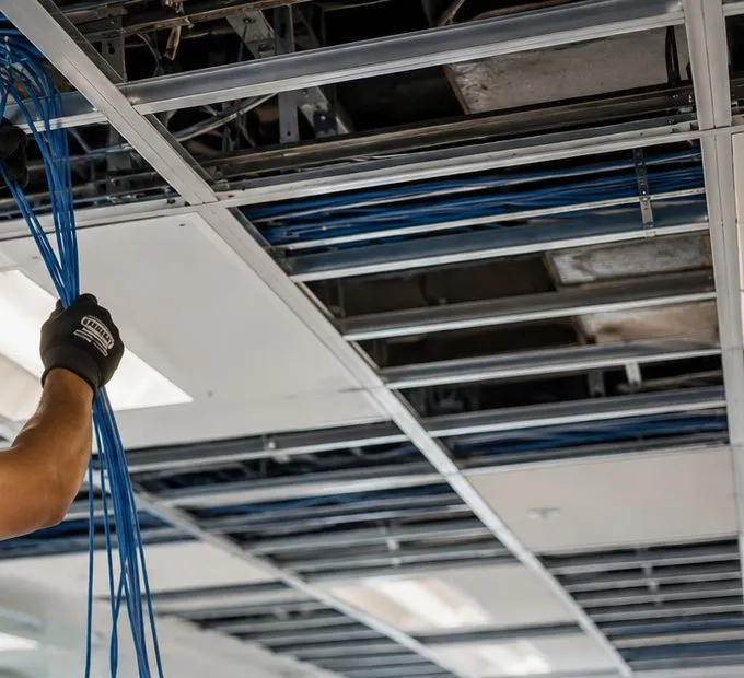 Blue cables drawn down through a ceiling grid — Park Slope, Brooklyn Sonos cable pull Cable pull for Sonos speakers in Park Slope, Brooklyn: a gloved hand drawing loose blue cables down through an open ceiling grid, with more cable running in the ceiling void