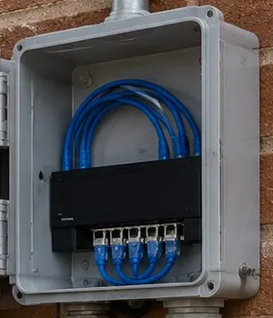 Open grey enclosure with blue cables on a brick wall — Riverdale, Bronx Sonos installation Sonos installation Riverdale, Bronx: open grey enclosure on brick with looped blue cables and a terminal block
