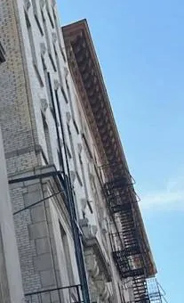 Iron fire escapes on an old apartment building — reference photo, Sonos installation St. George, Staten Island St. George, Staten Island Sonos installation reference photo: looking up an older brick and stone apartment building with black iron fire escapes and a deep cornice against blue sky