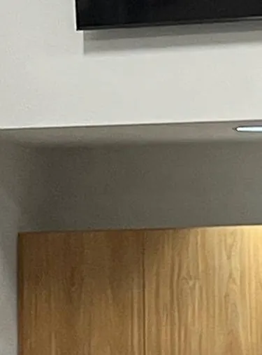 Bottom edge of a wall screen above a soffit and wood panel — reference photo, Sonos installation St. George, Staten Island St. George, Staten Island Sonos installation reference photo: bottom edge of a dark wall-mounted screen above a white soffit with a small light and a pale wood panel below