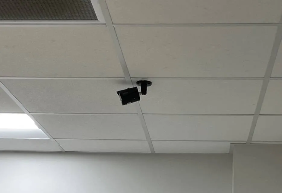 Throgs Neck, Bronx Sonos installation reference photo: white suspended ceiling grid with a small black camera on a bracket where the ceiling meets a plain white wall