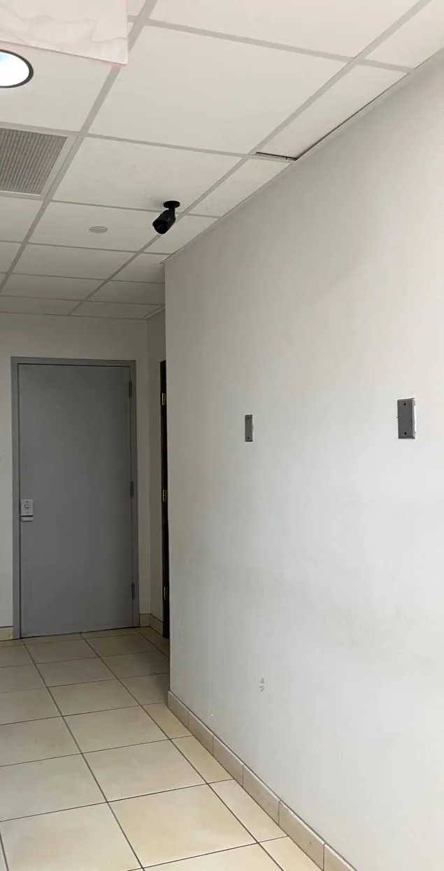 Throgs Neck, Bronx Sonos installation reference photo: white corridor wall with two small blank cover plates, a grey door at the end and a drop ceiling with a small camera