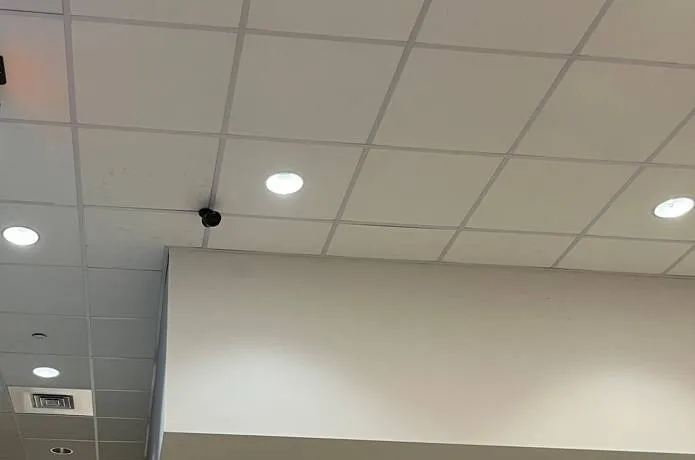 Throgs Neck, Bronx Sonos installation reference photo: white grid ceiling with round recessed downlights and a small black camera above the edge of a dropped soffit
