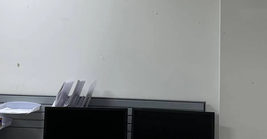 Blank wall above two dark monitors — reference photo from another AESS job, Sonos Upper West Side, Manhattan Upper West Side, Manhattan Sonos reference photo: plain white wall above the tops of two switched-off monitors and a stack of paper trays