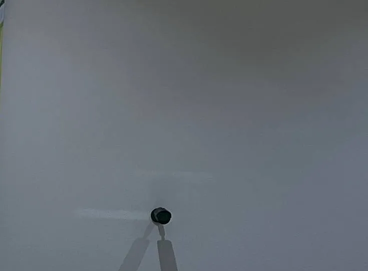 Small bracket-mounted device on a wide grey wall — AESS reference photo, Sonos installation Upper West Side, Manhattan Upper West Side, Manhattan Sonos reference photo: small black device on a short bracket in the lower middle of a wide pale grey wall
