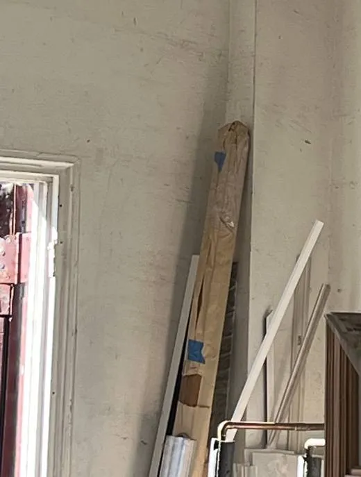 Lumber and trim leaning in a storeroom corner โ reference photo, Sonos installation Williamsburg, Brooklyn Williamsburg, Brooklyn Sonos installation reference photo from another AESS job: wrapped lumber and white trim boards leaning in the corner of a scuffed storeroom beside a window