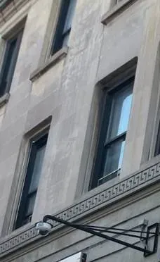 Dome camera on a steel wall arm below stone windows β Putnam County Ubiquiti installation example Putnam County Ubiquiti installation example photo: a small dome camera hanging from a black steel wall arm on a pale stone building below tall windows