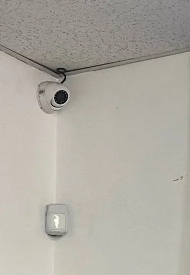 Small dome camera in a corner above a wall sensor β Putnam County Ubiquiti installation example Putnam County Ubiquiti installation example photo: a small white dome camera in the corner where a speckled ceiling meets white walls, with a wall sensor below