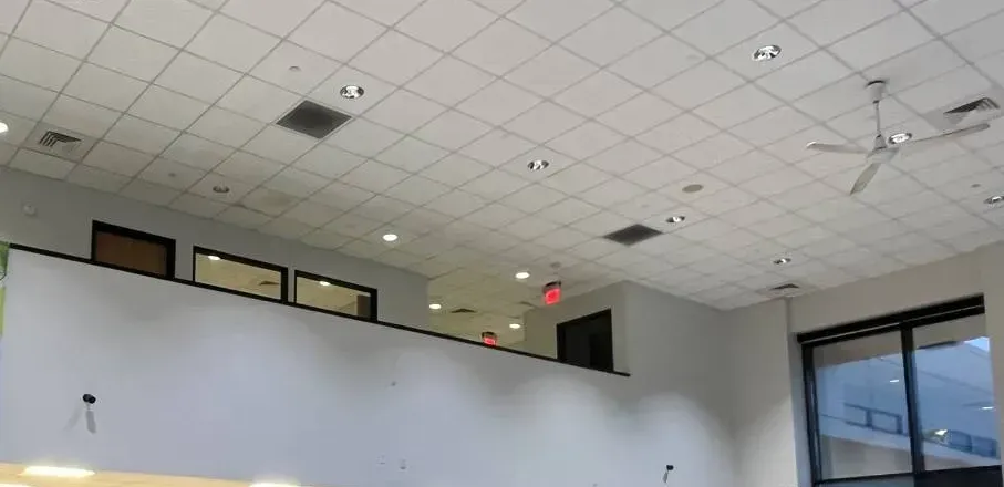 Two small cameras on a high wall below mezzanine windows β Putnam County Ubiquiti installation example Putnam County Ubiquiti installation example photo: two small black cameras on a tall white wall below mezzanine windows in a room with a drop ceiling and ceiling fan