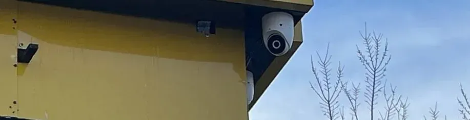 Box camera and dome camera on one painted eave corner — Dutchess County Uniview installation example Two cameras on a painted eave corner beside bare trees — Uniview camera installation Dutchess County example photo