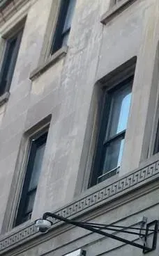Dome camera on a steel arm beneath a carved stone band â Manhattan Uniview facade reference Manhattan Uniview camera installation reference photo: a small dome camera on a long black steel wall arm, mounted below a carved stone band with a repeating key pattern on a grey masonry facade