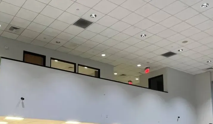 Two small cameras on a tall white wall below mezzanine windows â Manhattan Uniview reference Uniview camera Manhattan installation reference photo: two small cameras mounted on a tall white wall below a row of mezzanine windows, under a tiled ceiling with recessed lights and lit exit signs